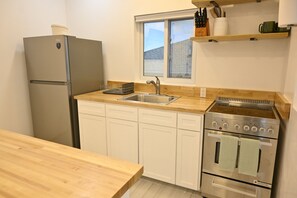 A compact kitchen with a refrigerator, sink, stove, and wooden countertop. - Emerald Cottage - Brand New Beach Cottage With Pool, Walk To La 1 Bedroom Home (North Palmetto Point)