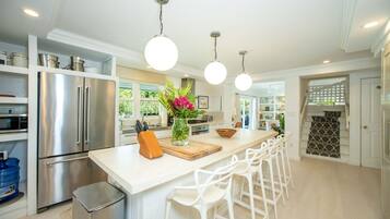 A modern kitchen with stainless steel appliances, a central island with bar stools, pendant lighting, and a view of the outdoors.