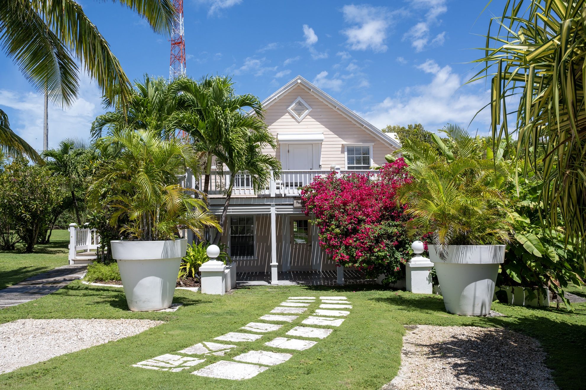 A two-story house with a balcony, surrounded by lush greenery and a well-maintained lawn.