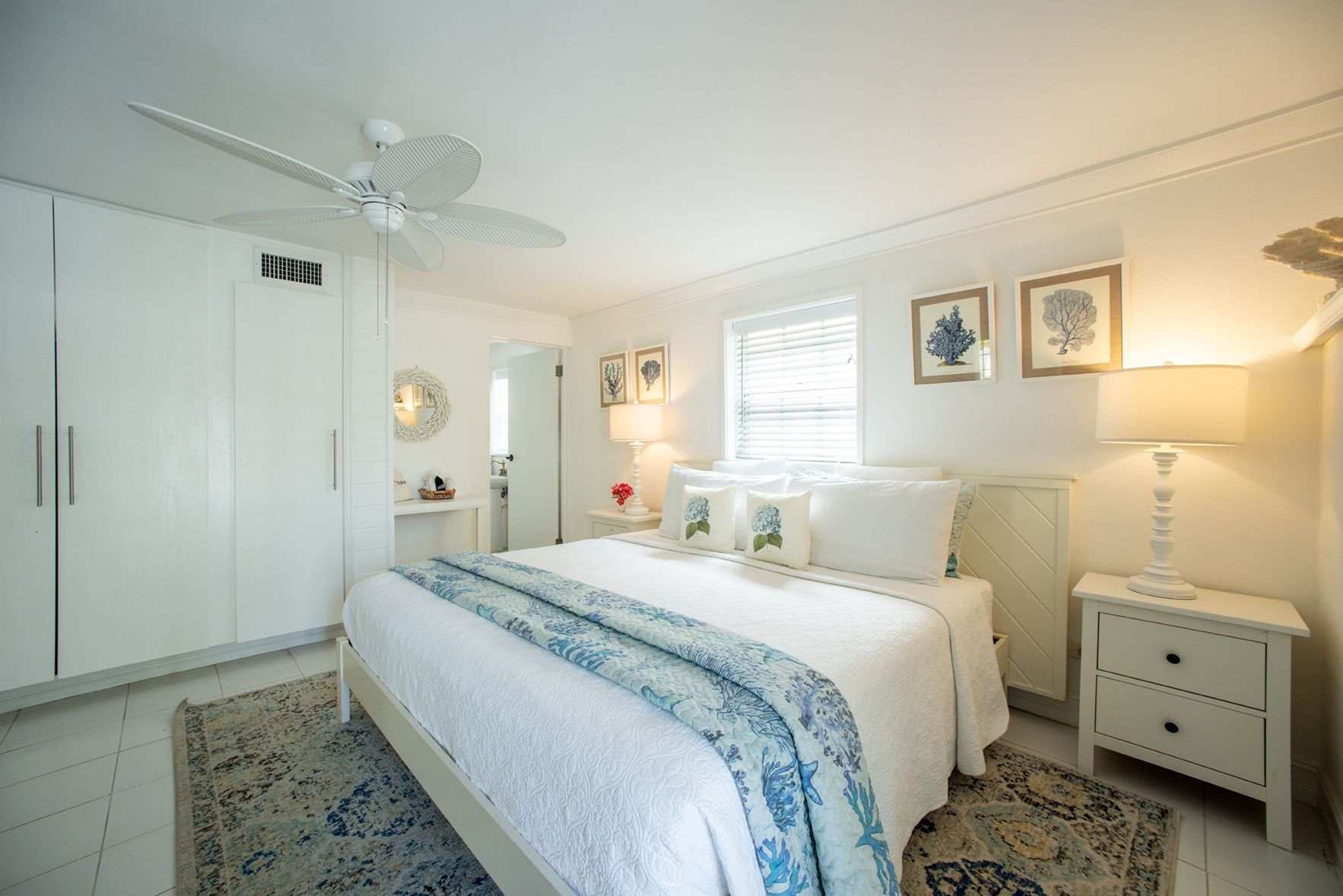 A bedroom with a bed, a nightstand, a lamp, a ceiling fan, and a window with blinds.