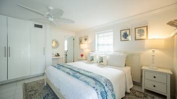 A bedroom with a bed, a nightstand, a lamp, a ceiling fan, and a window with blinds.