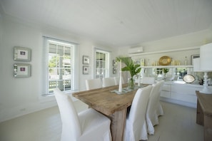 A dining area with a wooden table, white chairs, and a vase with plants. - Buena Vista Estate - Historic Estate Private Pool, Golf Cart 6 Bedroom Home (Governor's Harbour)