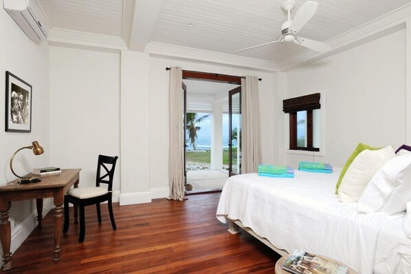 Ein Schlafzimmer mit Bett, Schreibtisch, Stuhl und einem Fenster mit Blick auf den Strand.