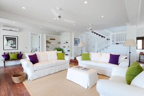 Ein geräumiges Wohnzimmer mit weißen Sofas, einem Couchtisch und einer Treppe, die in ein Obergeschoss führt.