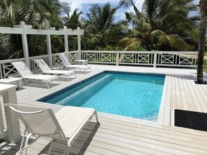Ein rechteckiger Swimmingpool mit Holzdeck und weißen Geländern, umgeben von Palmen.