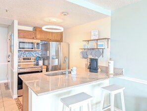 A kitchen with stainless steel appliances, a marble countertop, and a bar area with stools. - Ocean Front 2 BR | Myrtle Beach Resort - RT1902 (Myrtle Beach)