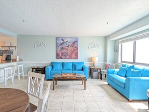 A living room with a blue sofa, a coffee table, and a painting of sea turtles. - Ocean Front 2 BR | Myrtle Beach Resort - RT1902 (Myrtle Beach)