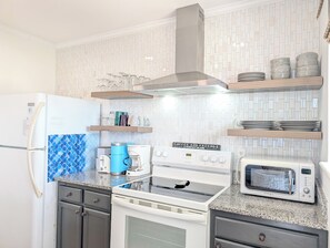 A kitchen with a refrigerator, stove, microwave, and shelves with kitchenware. - Ocean View 2 BR Condo | Myrtle Beach Resort RT0212 (Myrtle Beach)