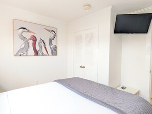 A bedroom with a bed, a painting of birds, a white door, and a television on the wall. - Ocean View 2 BR Condo | Myrtle Beach Resort RT0212 (Myrtle Beach)
