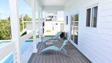 A covered outdoor area with a pool, lounge chairs, and a view of a neighboring building.
