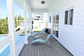 A covered outdoor area with a pool, lounge chairs, and a view of a neighboring building. - Crystal Cottage - Brand New Beach Cottage With Pool, Walk To La 1 Bedroom Home (North Palmetto Point)