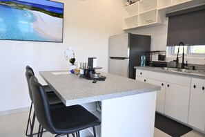 Eine moderne Küche mit einer zentralen Kochinsel, weißen Schränken und einem an der Wand montierten Flachbildfernseher.