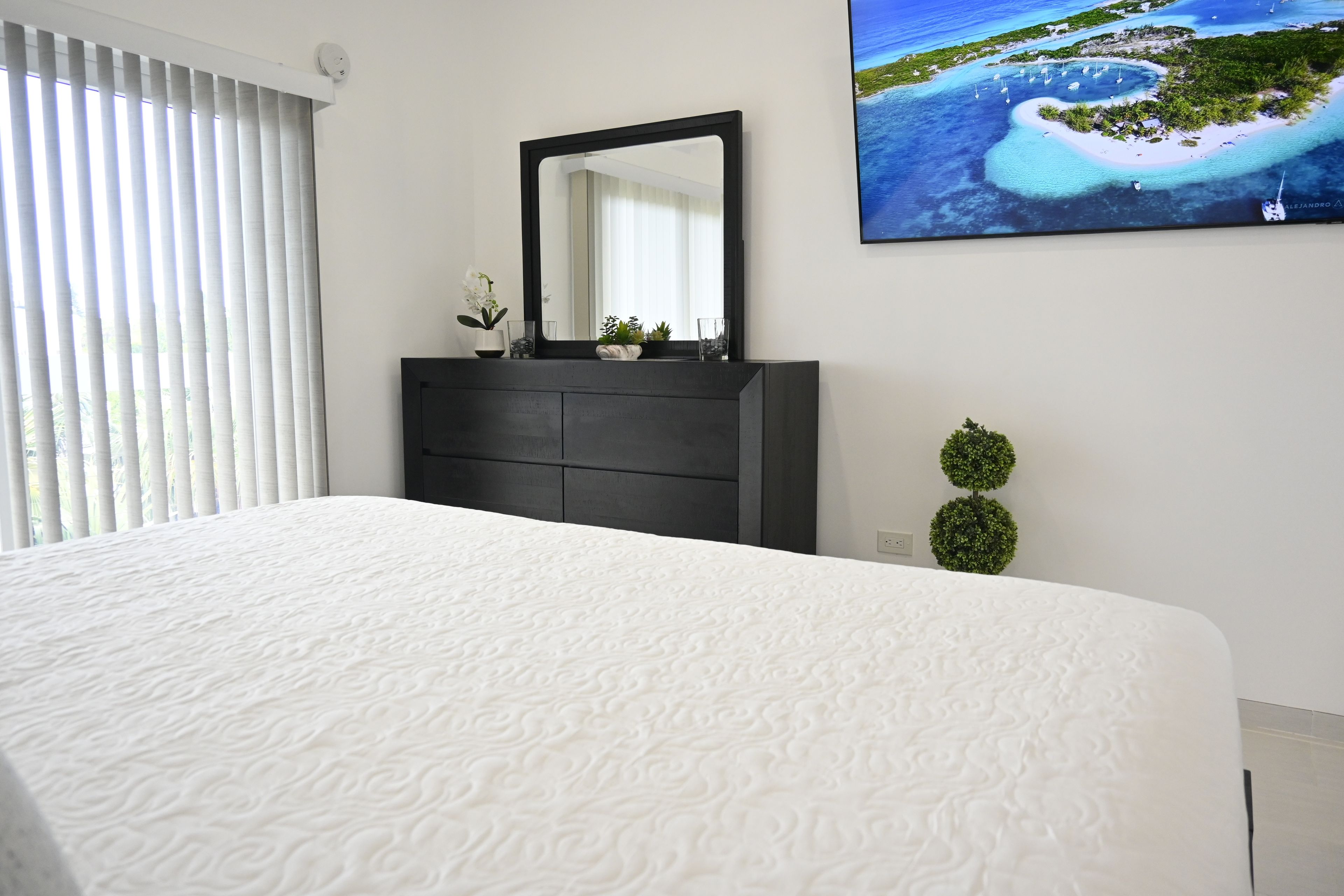 A bedroom with a bed, a dresser, a mirror, and a window with blinds.