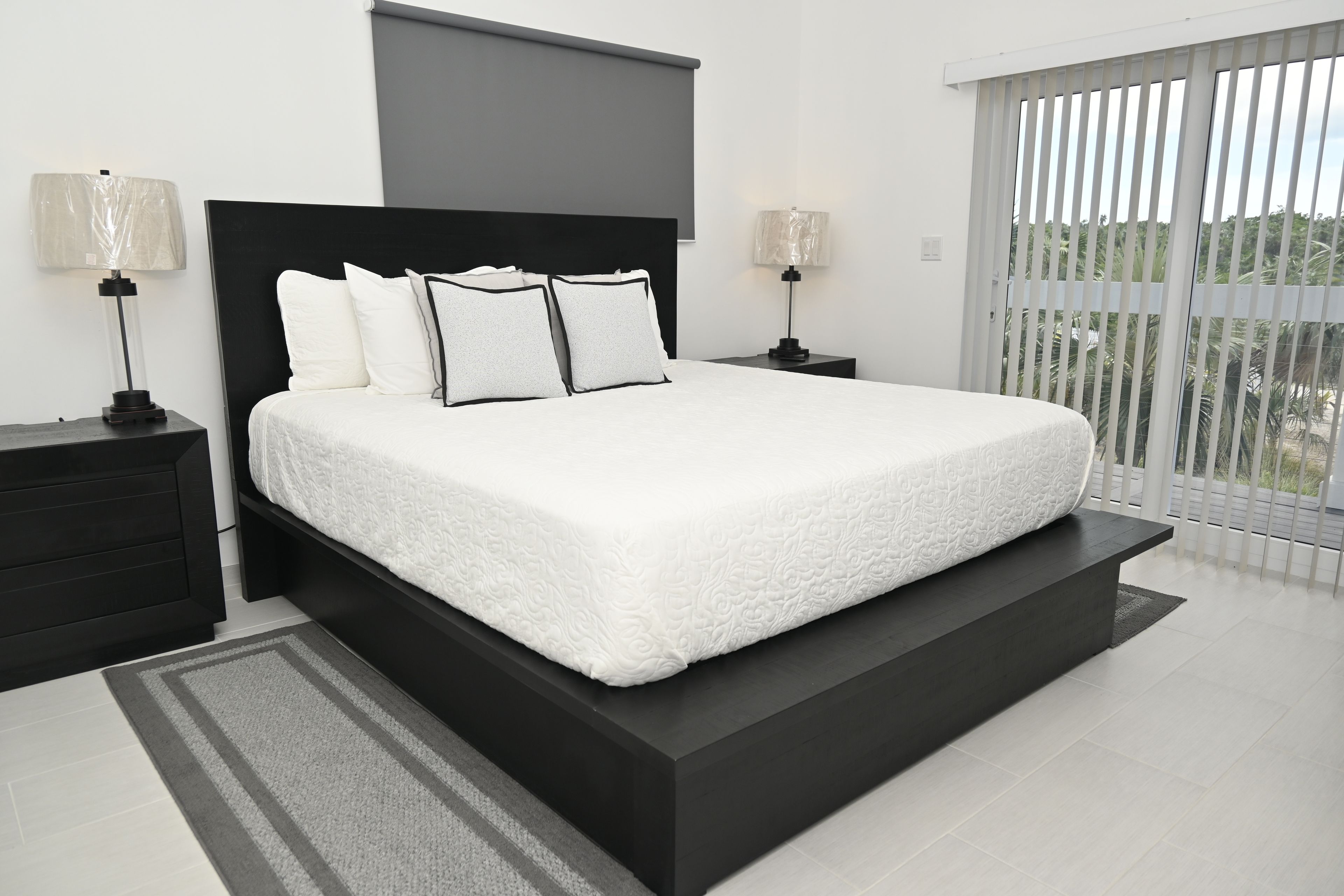 A modern bedroom with a large bed, two bedside tables, and a view of the outdoors through a sliding door.