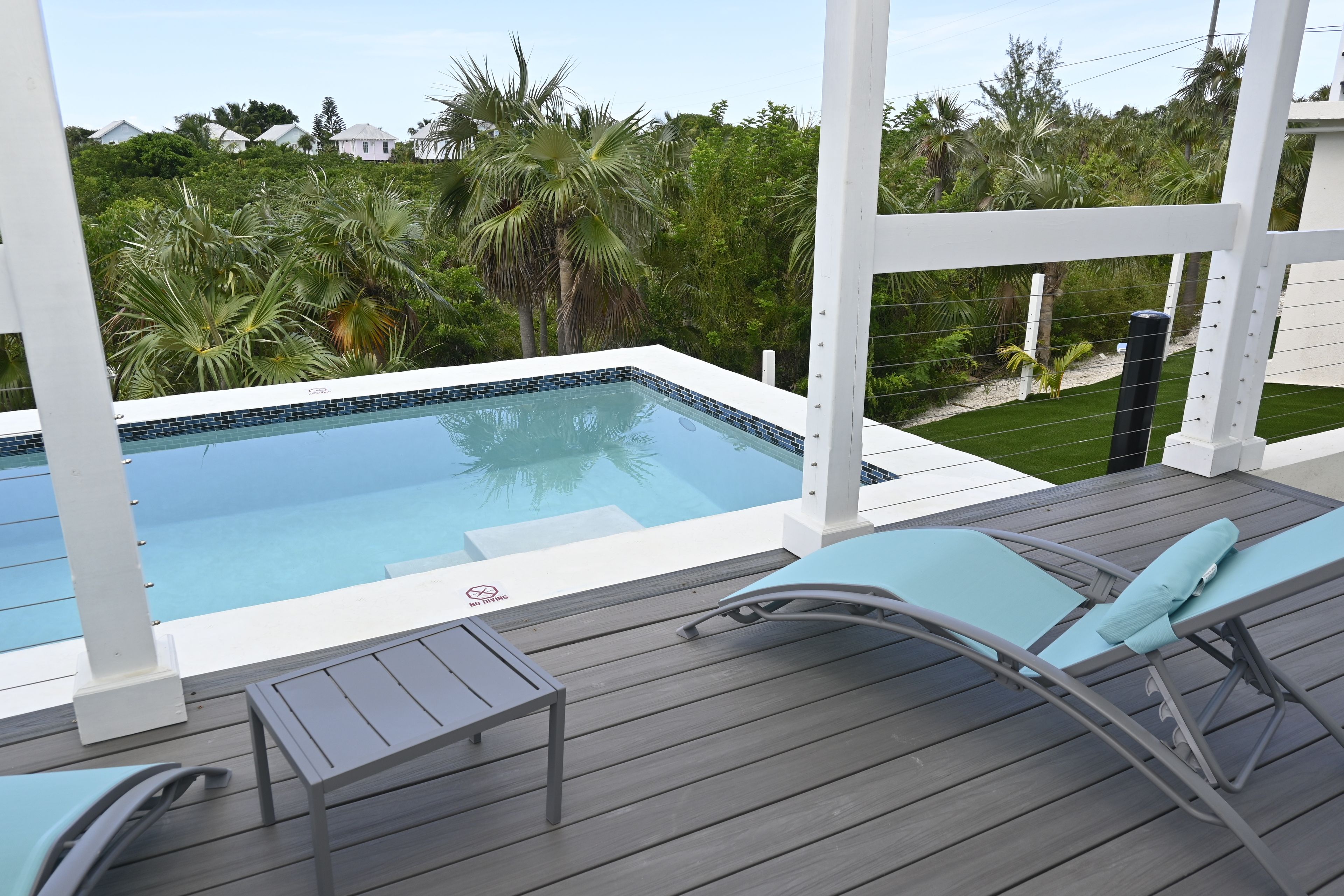 Ein Schwimmbecken mit einer gefliesten Kante, umgeben von einer Holzterrasse und zwei Liegestühlen.