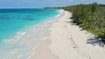 Uma praia com águas turquesa cristalinas, areia branca e vegetação densa à direita.