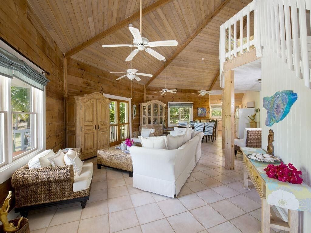 A spacious room with a high ceiling, multiple ceiling fans, a white sofa, a wicker sofa, and a dining area with a table and chairs.