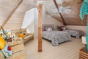 Um quarto de sótão aconchegante com teto inclinado, cama com roupa de cama estampada, sofá com almofadas coloridas e um ventilador de teto.