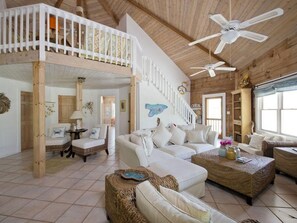 A spacious living area with a high ceiling, white furniture, and a balcony with a railing. - Shangri-la & Cottage · Tropical Beach Villa With Guest Cottage 5 Bedroom Villa (Governor's Harbour)