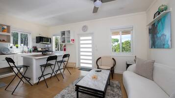A modern kitchen with a central island, dining chairs, a sofa, and a ceiling fan.