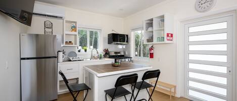 A compact kitchen with a refrigerator, stove, microwave, and a small dining area with chairs.