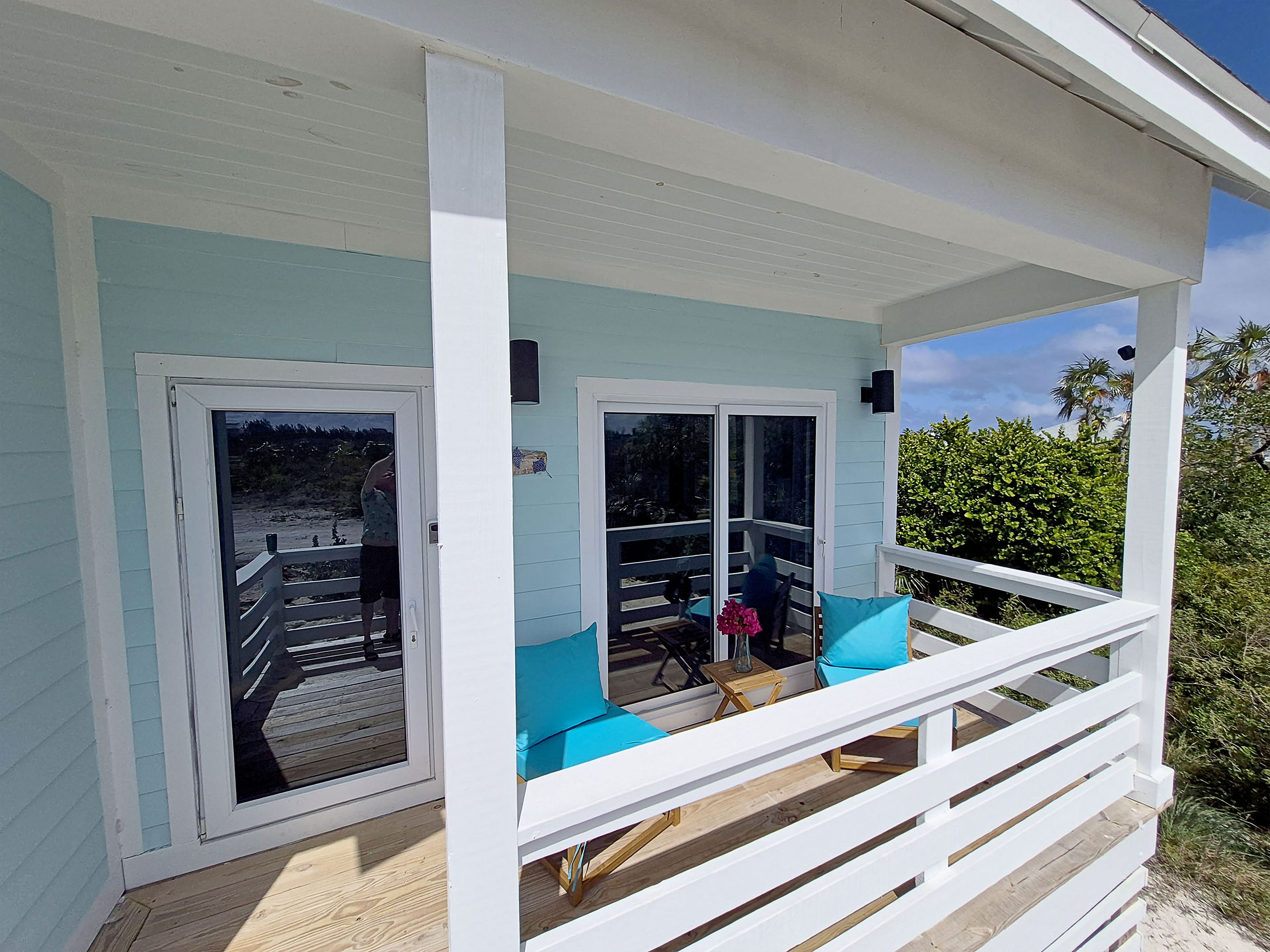 Un espace extérieur abrité doté d’une terrasse en bois, de deux portes-fenêtres coulissantes et d’une rambarde blanche.