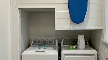 A laundry room with two washing machines, a drying rack, and a window.