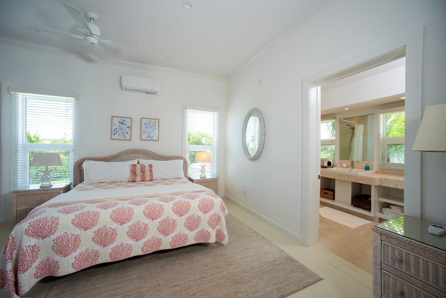A bedroom with a bed, bedside tables, a ceiling fan, and a bathroom with a mirror, sink, and shower.