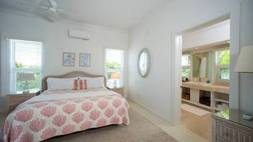 A bedroom with a bed, bedside tables, a ceiling fan, and a bathroom with a mirror, sink, and shower.