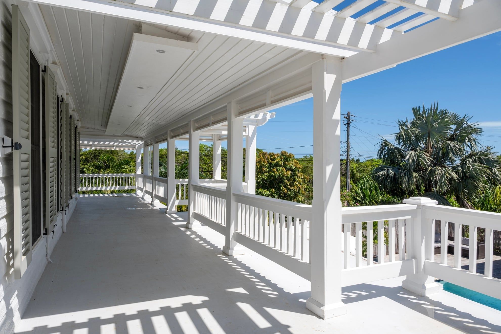 A covered porch with white railings, a concrete floor, and a view of palm trees and greenery.