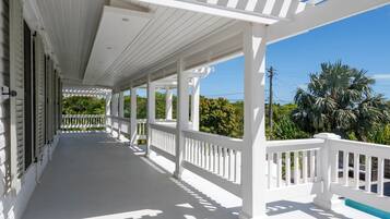 A covered porch with white railings, a concrete floor, and a view of palm trees and greenery.