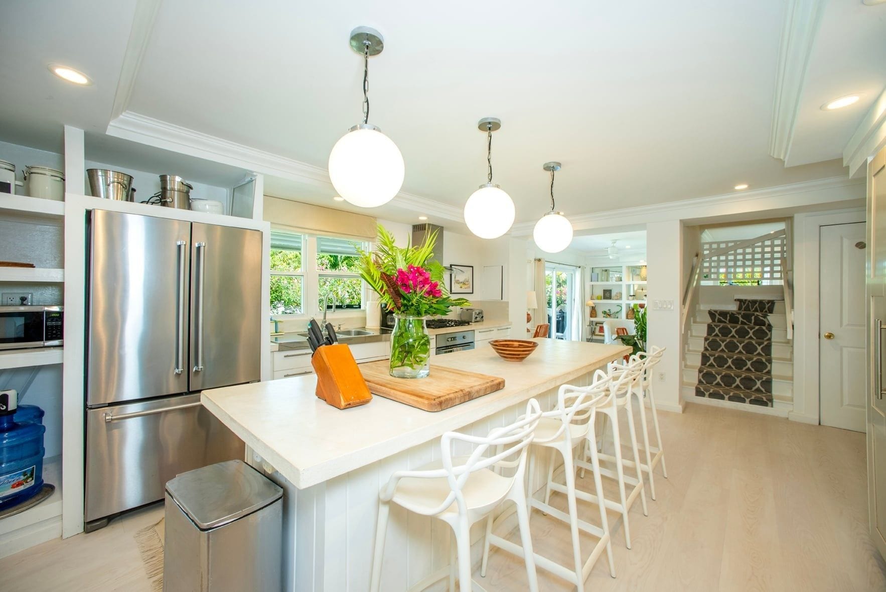 A modern kitchen with stainless steel appliances, a central island with bar stools, pendant lighting, and a view to the outdoors.