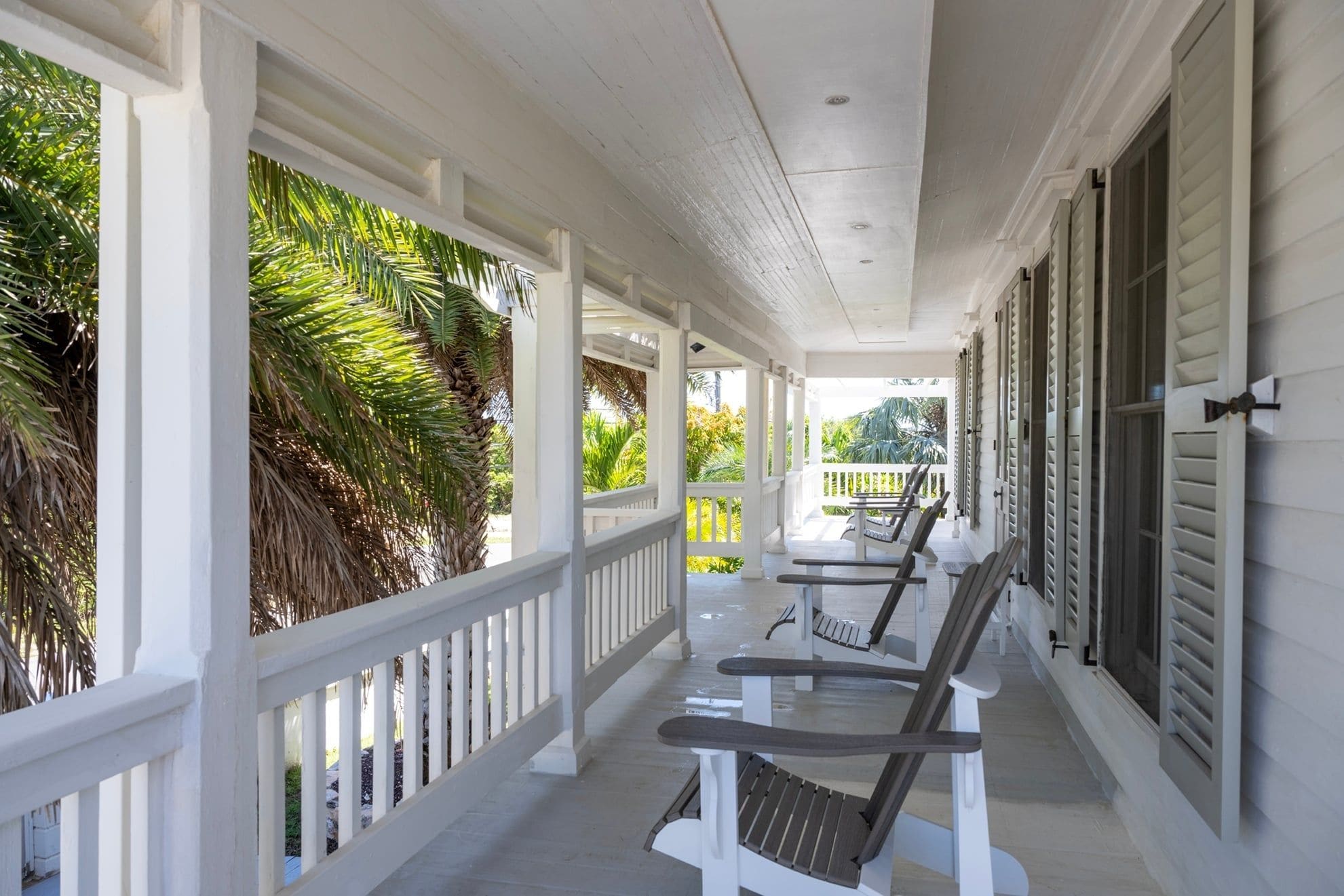 A covered porch with white railings, wooden chairs, and a table.
