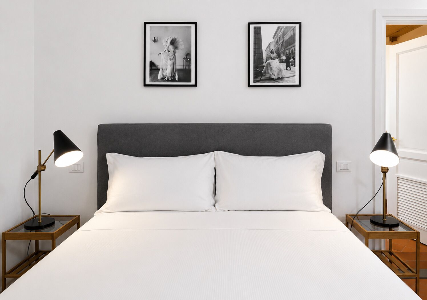Un lit avec du linge de lit blanc, une tête de lit sombre et deux tables de chevet avec des lampes.