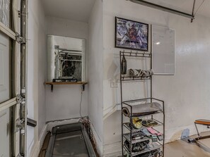 A room with a window, a metal shelf with items, a wall-mounted light switch, and a painting.
