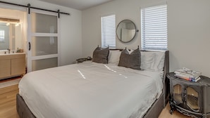 Quarto com cama, penteadeira, mesa de cabeceira com livros, espelho e porta de correr.