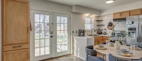 Una cocina moderna con armarios de madera, un comedor con mesa y sillas redondas, y vistas a través de puertas de vidrio.