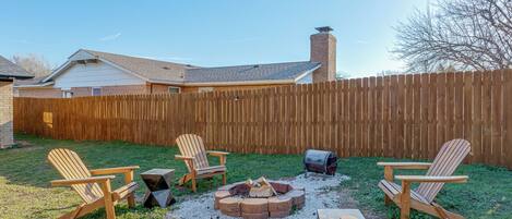 A backyard with a wooden deck, outdoor seating, and a fire pit.