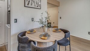 Mesa redonda para refeições com quatro cadeiras, vaso com planta e quadro na parede.