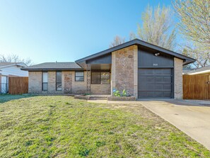 A residential house with a garage, a stone facade, and a well-maintained lawn. - 3-bedroom home in charming Midwest City with AC and fitness room (Midwest City)