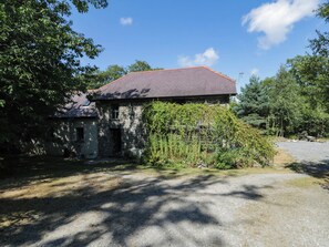 A stone building with a red roof, surrounded by greenery and a gravel driveway. - Yr Hen Felin (Boncath)