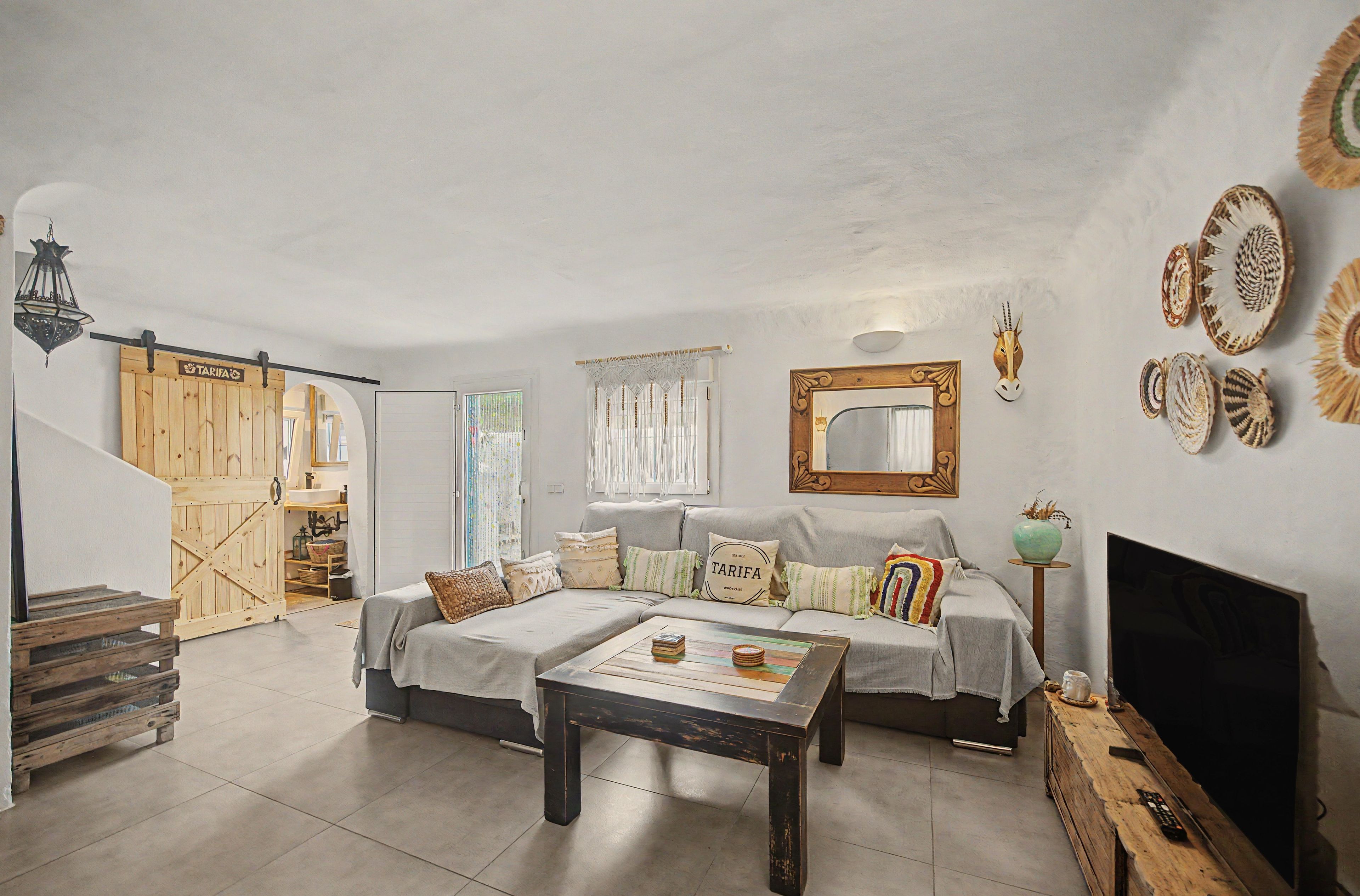 A living room with a sofa, a coffee table, a television, and a wall-mounted mirror.
