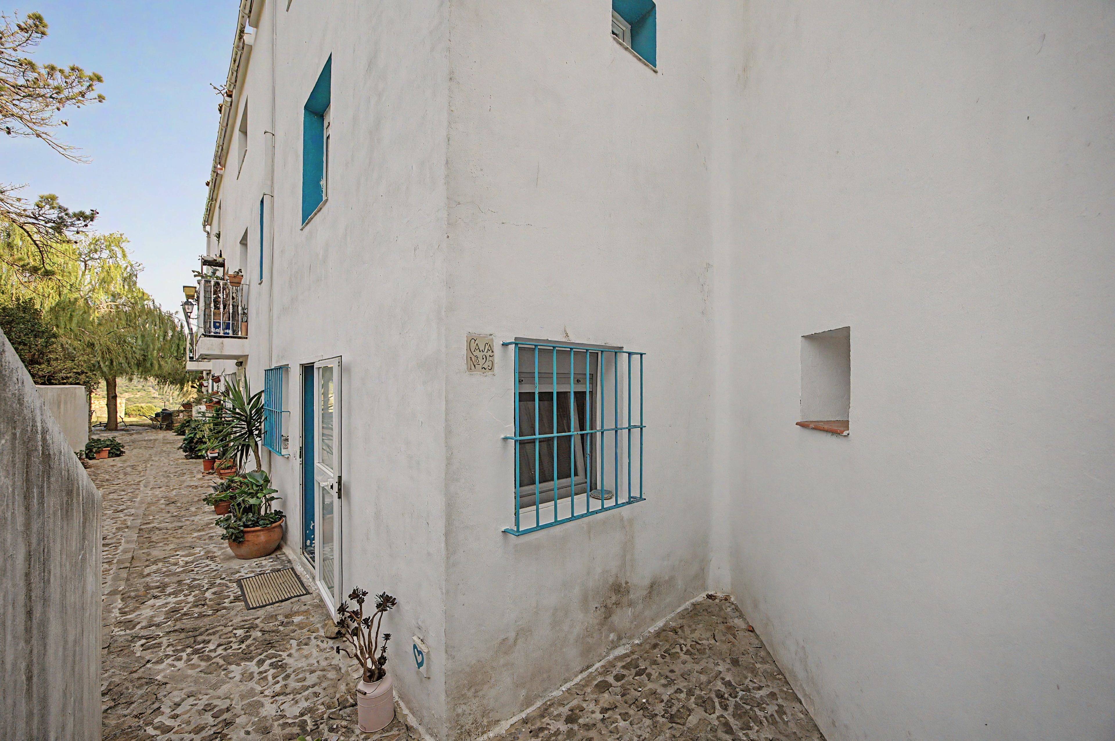 A narrow cobblestone street flanked by white buildings with blue window frames and shutters.