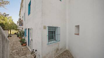 A narrow cobblestone street flanked by white buildings with blue window frames and shutters.