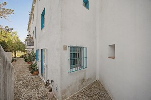 A narrow cobblestone street flanked by white buildings with blue window frames and shutters.