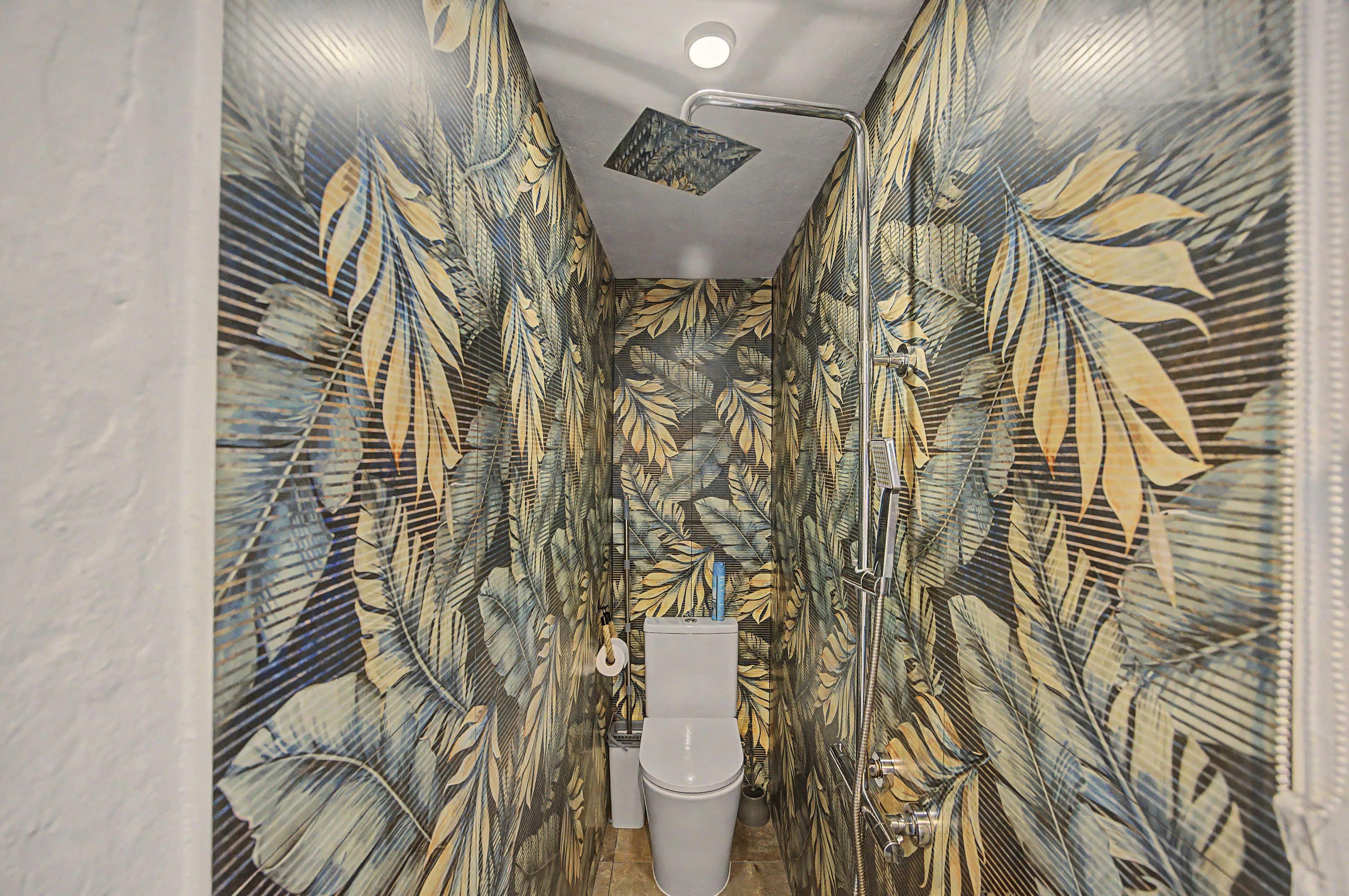 A bathroom with a shower, toilet, and sink, all enclosed by walls with a tropical leaf pattern.