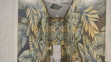 A bathroom with a shower, toilet, and sink, all enclosed by walls with a tropical leaf pattern.