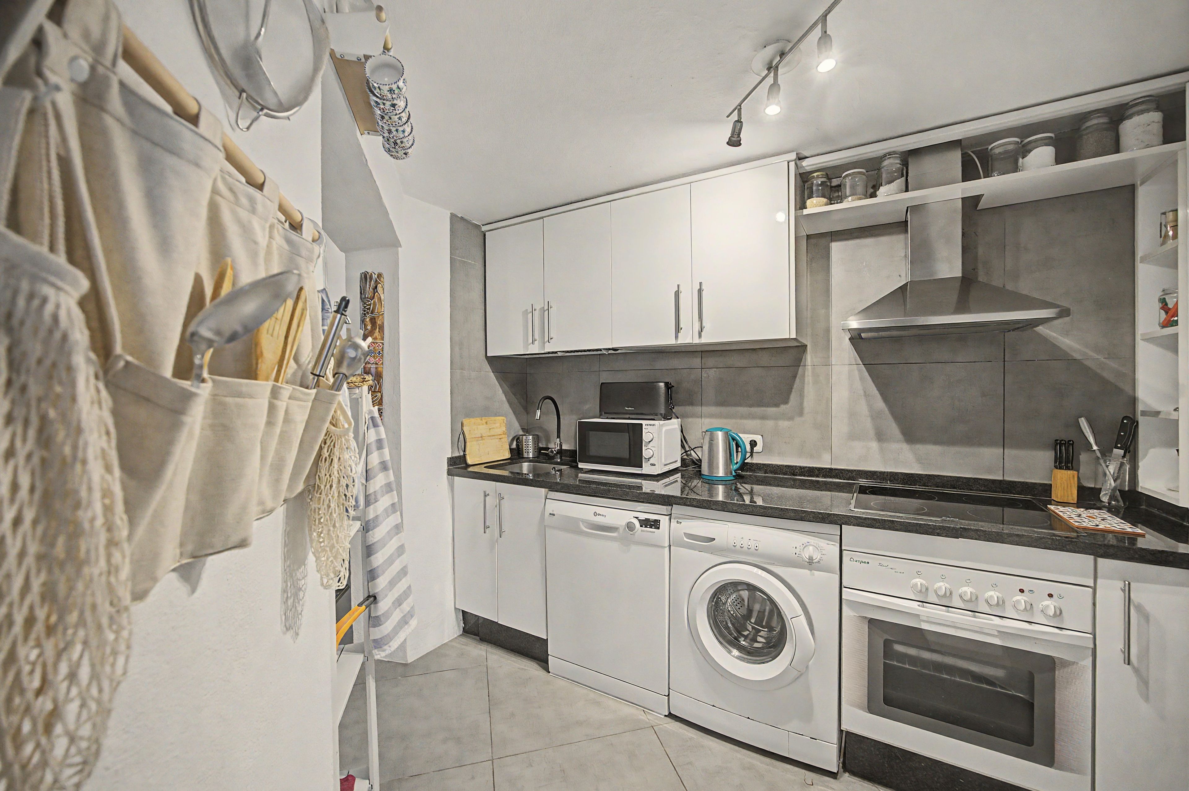 Une cuisine moderne avec des meubles blancs, un four encastré, un four à micro-ondes et un lave-linge.