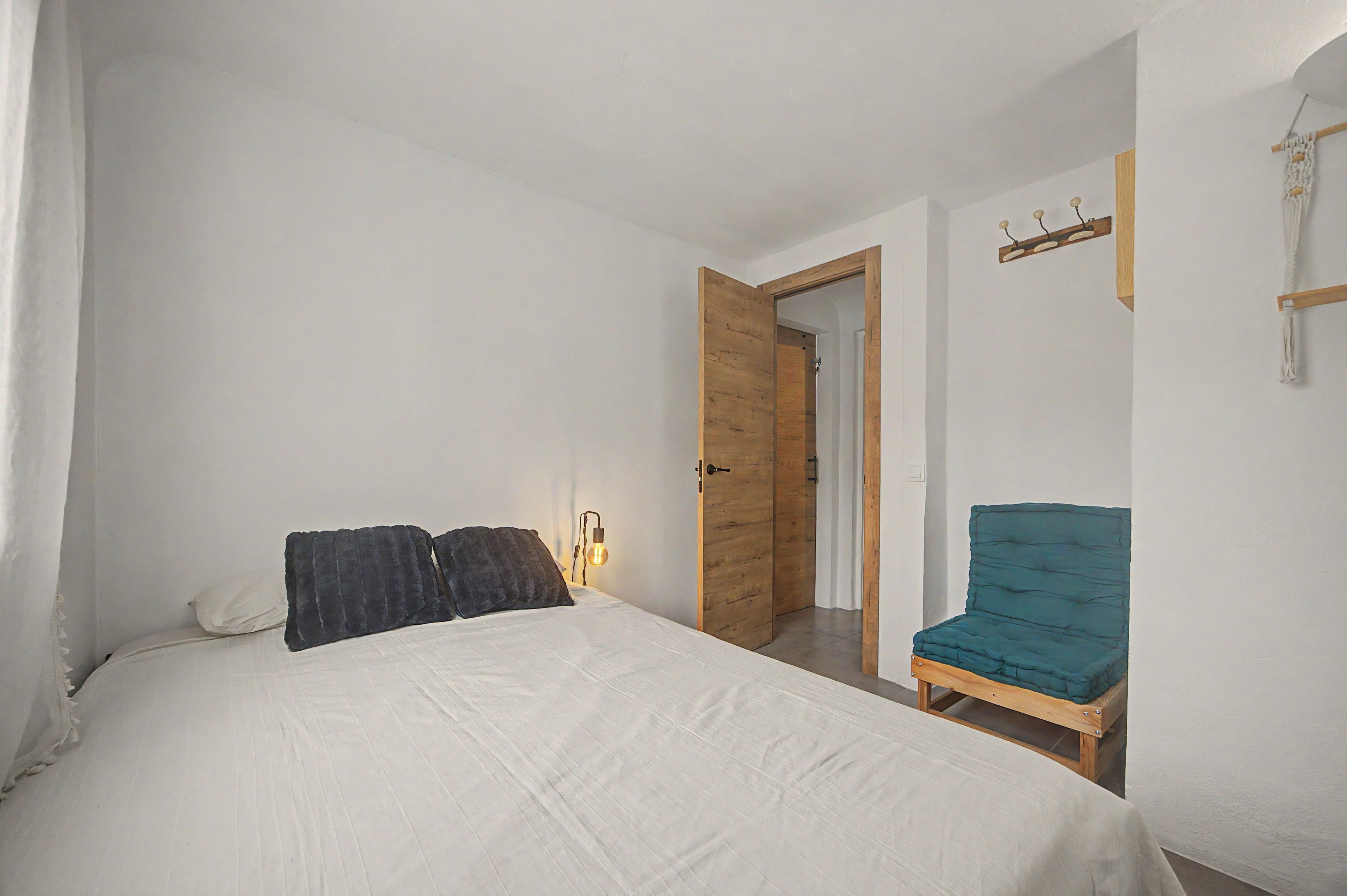 A bedroom with a bed, a chair, a wooden door, and a wall-mounted light fixture.