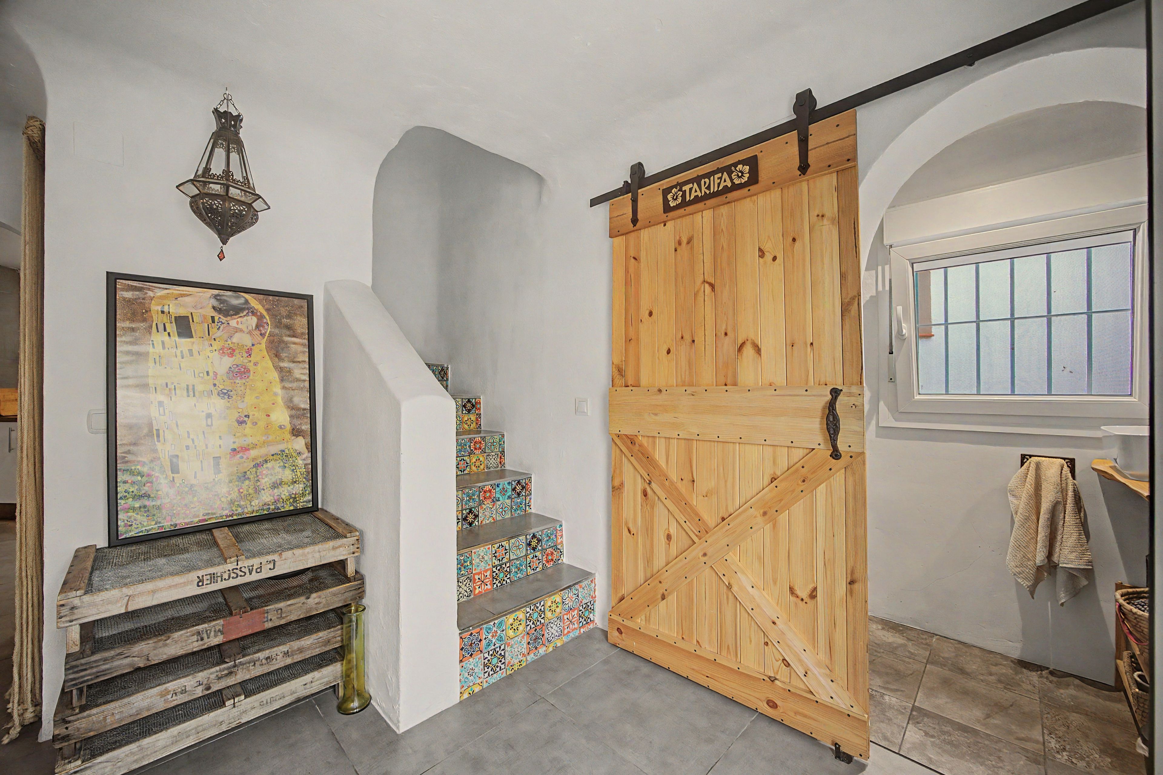Eine Treppe mit farbenfrohen Fliesen, eine mit 'TARIFA' beschriftete Holztür und ein gerahmtes Gemälde an der Wand.